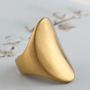 Macro detail of golden oval shield ring featuring a heavy brushed metal finish