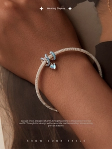Detailed view of silver mesh bracelet with blue enamel charms and heart pendant on wrist