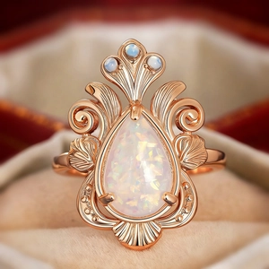 Macro view of teardrop opal ring in rose gold with vintage filigree and blue accent stones