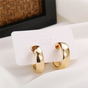 Macro detail of glossy gold C-shaped hoop earrings on jewelry card with 925 silver post