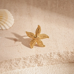 Close-up of golden starfish ear clip with granular texture on a beige stone surface