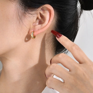 Close-up of gold hoop earring with three white zircons on model ear profile view