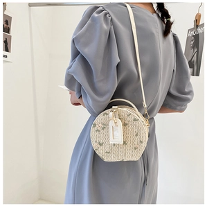 Detail of round straw crossbody bag with pink floral embroidery and white PU leather strap