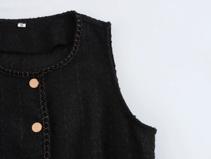 Dettaglio dello scollo in tweed con catena dorata e bottoni metallici in primo piano