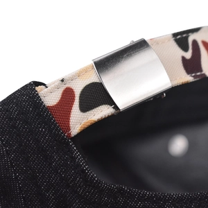 Detail of adjustable camouflage canvas strap and silver metal buckle on a black denim hat