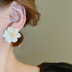 Detailed view of white resin camellia stud earring with golden stamen on female model