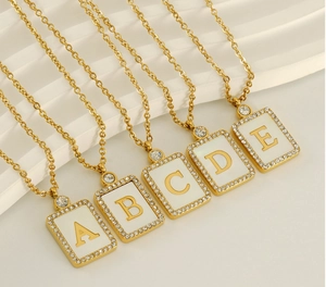 Close-up of golden rectangular letter pendants A to E with rhinestones and white shell inlay