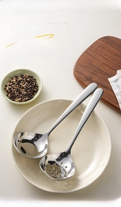Polished stainless steel soup ladle and slotted spoon set displayed on a beige plate
