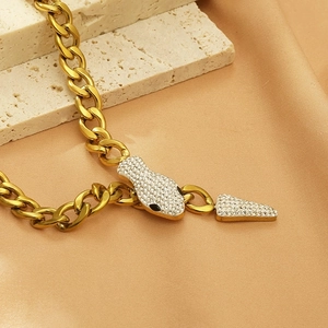 Macro detail of gold snake-shaped pendant with white crystals and chunky curb chain