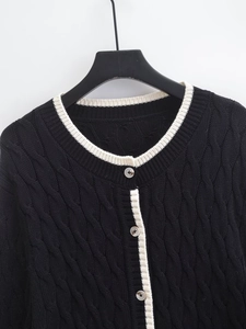 Close-up of black cable knit cardigan with contrasting white trim and round buttons