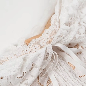 Detailaufnahme weißer Spitzendetails mit Bogenkante und Band am Minikleid aus Spitze