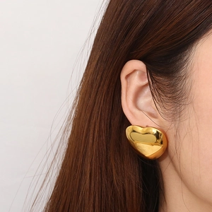 Close-up of 18K gold-plated hollow heart stud earrings on model's ear showing polished finish