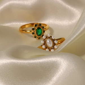Detail of luxury emerald and pearl gold rings displayed on elegant beige silk fabric