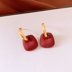 Macro shot of gold hoop earrings featuring matte burgundy trapezoid pendants on leather