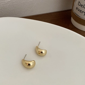 Minimalist gold pea stud earrings with polished curved surface on a wooden table