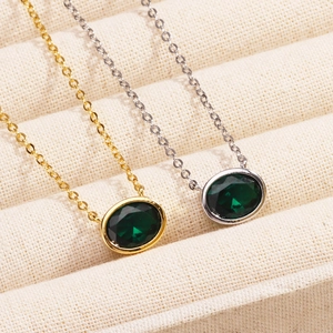 Detailed view of gold and silver necklaces with oval emerald pendants in a jewelry box