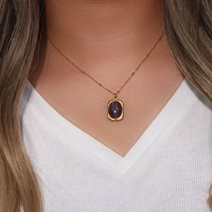 Detail of a vintage gold oval necklace with a purple stone pendant on a model