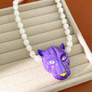 Vue détaillée du pendentif tête de panthère violette avec collier de perles blanches