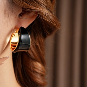 Detail of vintage C-shaped resin earrings in black and gold plating worn by model