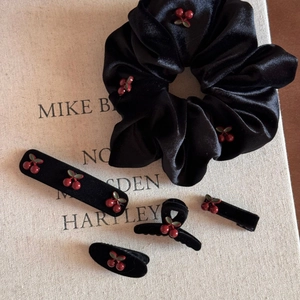 Flat lay of black velvet hair accessories set with cherry embroidery on book pages