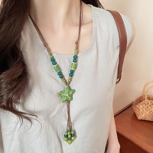 Close-up of a green ceramic starfish pendant with beaded wax cord on a model