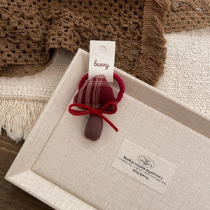 Detail of red checkered mushroom hair tie with a small bow on a beige linen box