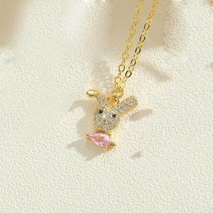 Macro detail of a golden rabbit pendant with micro-pave stones and a pink teardrop gem