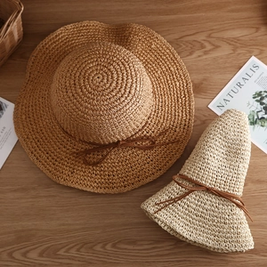 Breathable wide brim straw sun hat with bowknot detail shown in two colors on wood