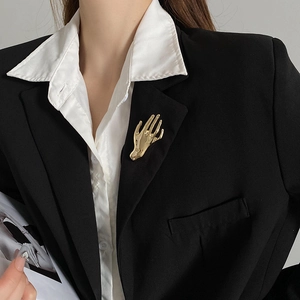Detail view of a creative gold hand brooch styled on a classic black suit jacket