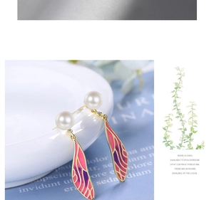 Detail view of long gradient wing earrings with pearls on a decorative white porcelain bowl