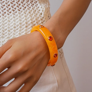 Close-up of orange acrylic resin bracelet with matching rhinestones worn by a model