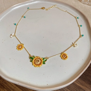 Detail of sunflower and bee necklace with turquoise beads on a ceramic plate