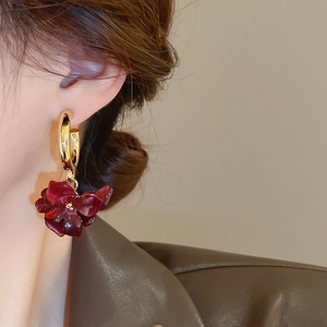 Close-up of model wearing dark red floral drop earrings with gold hoops and leather jacket