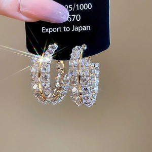 Détail de créoles dorées avec trois rangées de zircons étincelants de taille carrée