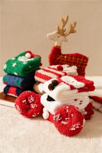 Close-up of thick coral fleece Christmas socks stacked on white plush background with decor