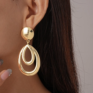 Macro shot of gold-plated teardrop layered earrings worn by a model in soft lighting