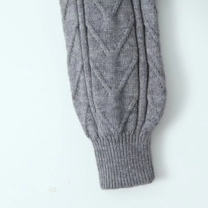 Macro detail of grey cable knit sleeve with textured diamond patterns and ribbed cuffs