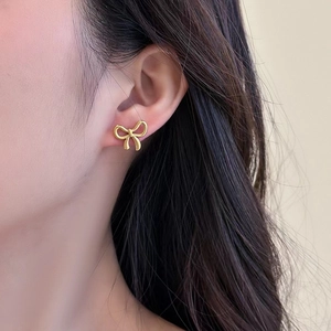 Elegant gold bow earrings in titanium steel for women worn by a professional model