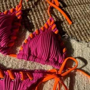 Detail of ribbed hot pink bikini with orange lace-up ties and silver metal eyelets