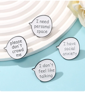 Close-up of four black and white speech bubble enamel pins with social anxiety quotes