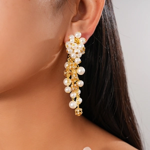 Detail of long drop earrings featuring white pearls and shimmering diamond-set golden spheres