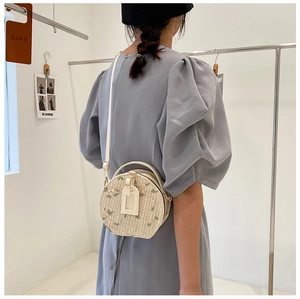 Detail of round straw crossbody bag featuring delicate pink floral embroidery and white leather