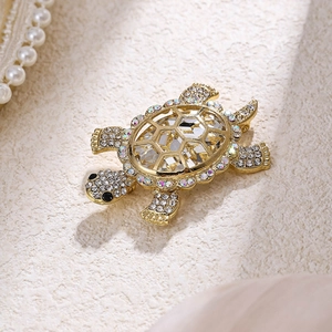 Fashionable gold turtle brooch with faceted crystals and rhinestones on a textured surface