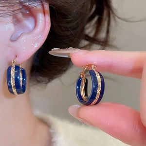 Close-up of deep blue enamel C-shaped earrings with gold trim worn by a model