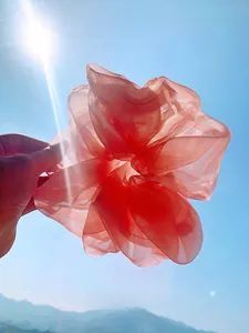 Close-up of coral organza scrunchie with layered pleats against a bright sky background