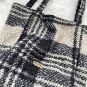 Close-up of black and white checkered faux shearling tote with gold metal brand tag