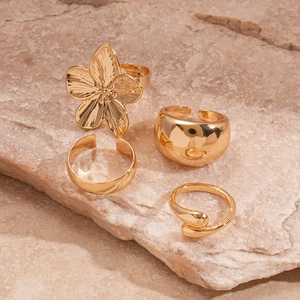 Three-piece gold metal geometric flower ring set displayed on a natural stone background