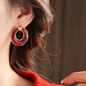 Close-up of elegant gold-toned earrings with red resin details worn by a model