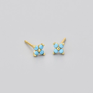 Detail of four-leaf flower studs with sky blue zircons and golden base on grey background