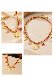 Macro detail of gold-plated sun and cherry pendants on a red woven string necklace